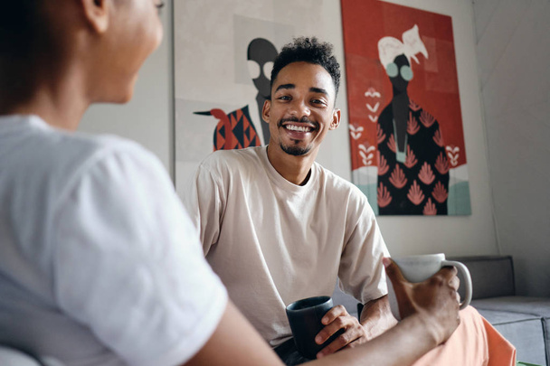 Mladý atraktivní úsměv ležérní Afroameričan muž radostně dívá do kamery během přestávky na kávu v moderním co-working prostoru - Fotografie, Obrázek