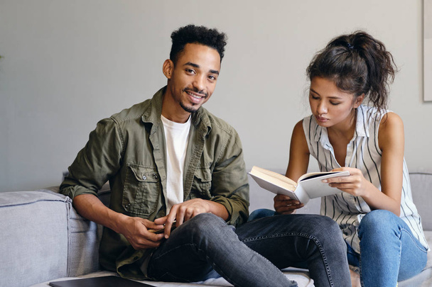 Young smiling African American man joyfully looking in camera while studying with Asian girl in modern co-working space - Zdjęcie, obraz