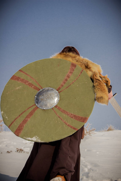 Une fille en costume de Valkyrie grimpe une montagne enneigée et tient une épée et un bouclier dans ses mains. Guerrière avec un bouclier. Valkyries dans la forêt d'hiver
. - Photo, image
