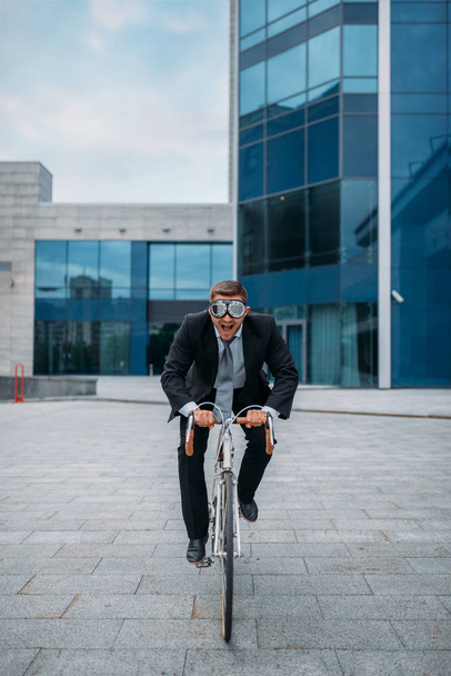 One businessman in funny glasses poses on bicycle at the office building in downtown. Business person riding on eco transport on city street - Photo, Image