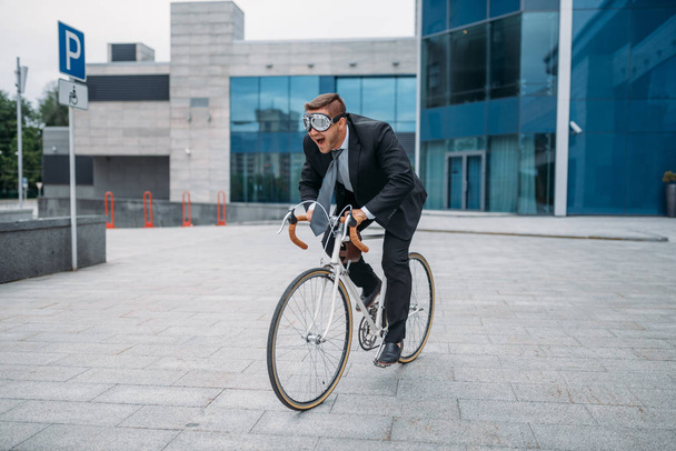 Ένας επιχειρηματίας με αστεία γυαλιά ποζάρει με ποδήλατο στο κτίριο του γραφείου στο κέντρο. Επιχειρηματίας ιππασία στις οικολογικές μεταφορές στο δρόμο της πόλης - Φωτογραφία, εικόνα