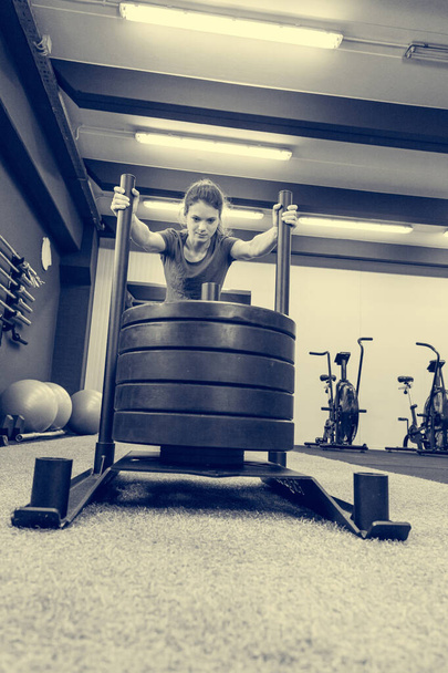 Young female fitness trainer performing sled push in local gym. - Photo, Image