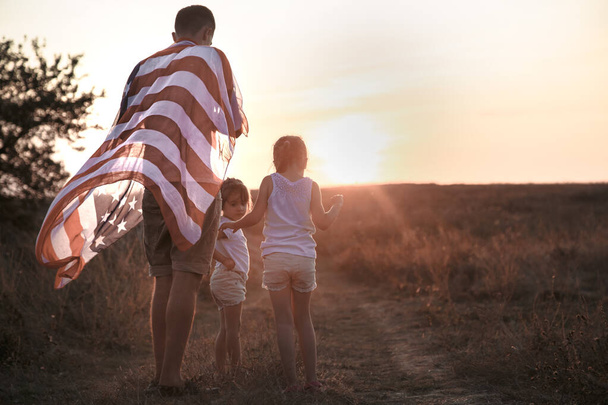 Щаслива родина з американським прапором на заході сонця. - Фото, зображення