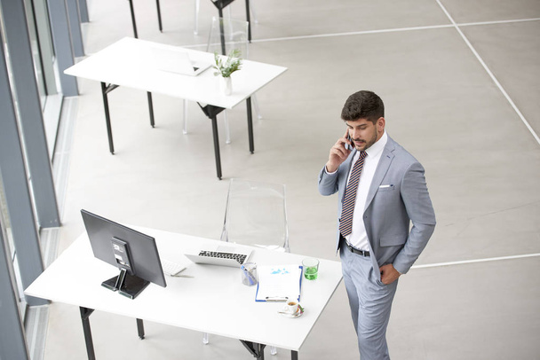 Elegant businessman making a call while standing at office desk  - Fotó, kép
