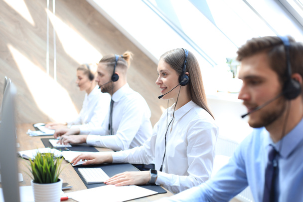 Female customer support operator with headset and smiling accompanied by her team. - Фото, зображення