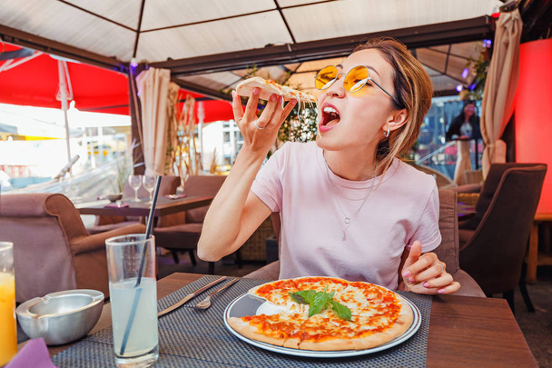 Young girl eating delicious pizza with cheese and greens in pizzeria - Foto, Imagem