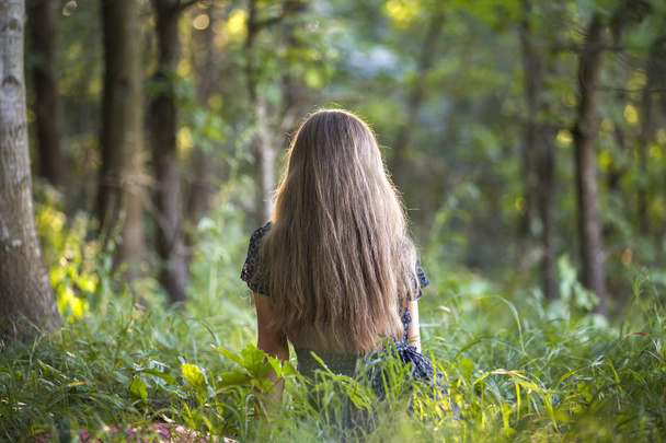 Вид ззаду жінки з довгим волоссям, що сидить на відкритому повітрі в лісі e
 - Фото, зображення