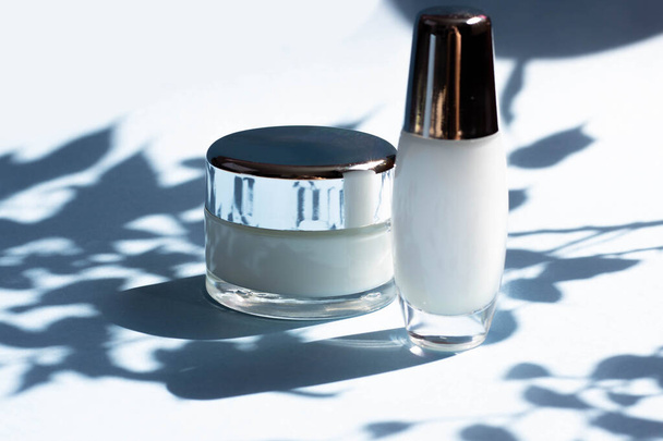 Face cosmetics. Jars of cream, face mask on a blue background with hard shadows from the leaves. Beauty blogger, procedures salon concept. Minimalism. - Valokuva, kuva
