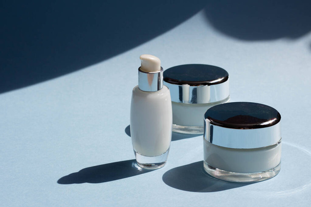 Face cosmetics. Jars of cream, serum and face mask on a blue background with hard shadows. Beauty blogger, procedures salon concept. Minimalism. - Fotó, kép