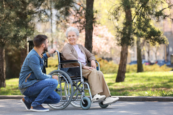 Senior woman in wheelchair with young man at park - Φωτογραφία, εικόνα