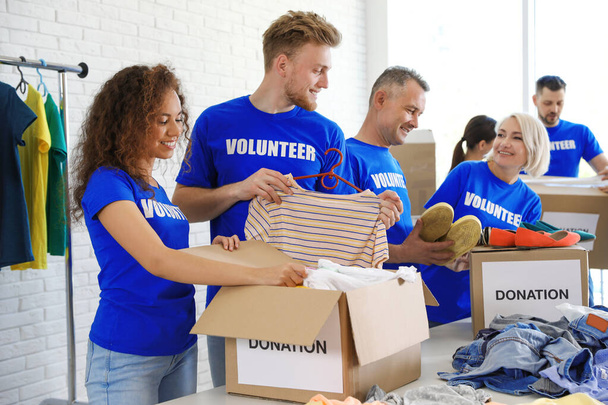 Vapaaehtoisten ryhmä, joka kerää lahjoituksia laatikoihin sisätiloissa
 - Valokuva, kuva