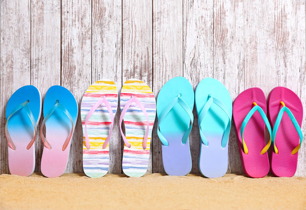 Different bright flip flops on sand near wooden wall, space for text. Summer beach accessories - Φωτογραφία, εικόνα