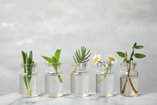 Glass bottles of different essential oils with plants on table - Zdjęcie, obraz