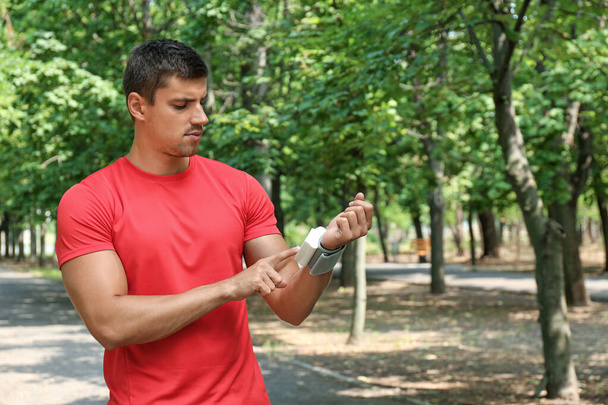 Young man checking pulse with medical device after training outdoors - Zdjęcie, obraz