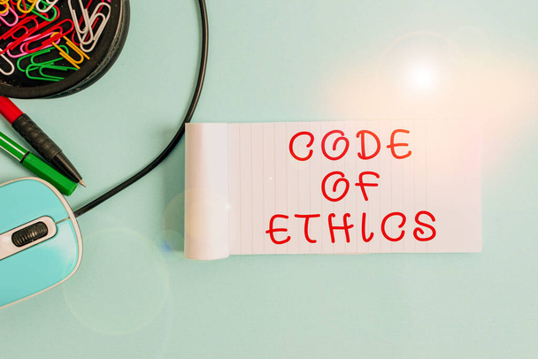 Handwriting text Code of Ethics Концепція означає основний посібник для професійної поведінки і нав'язує обов'язки Ноутбука і письмового обладнання з комп'ютерною мишкою над пастельним фоном. - Фото, зображення