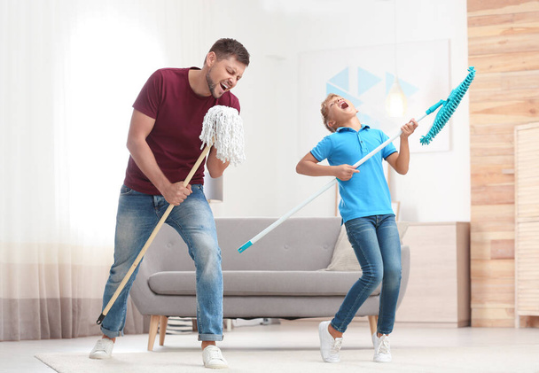 Dad and son having fun while cleaning living room together - 写真・画像