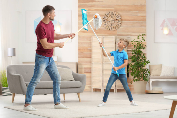 Dad and son having fun while cleaning living room together - Фото, изображение