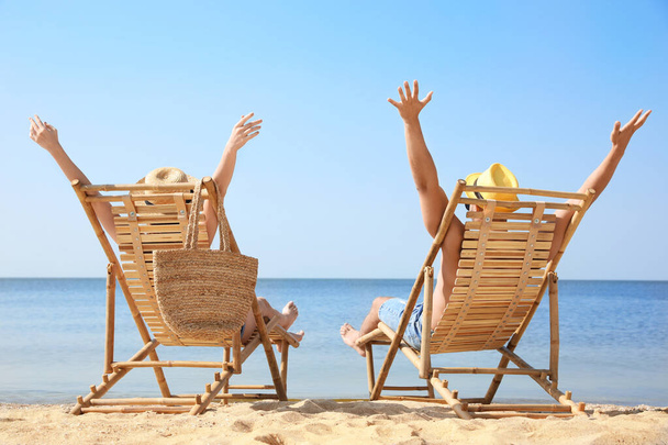 Young couple relaxing in deck chairs on beach - Foto, afbeelding