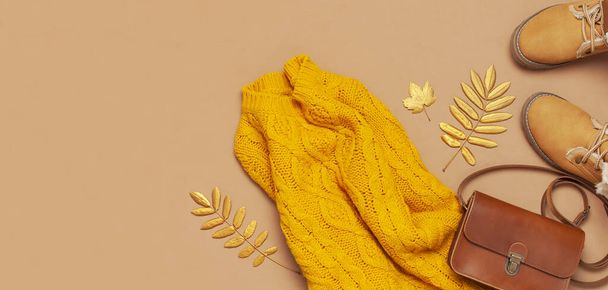 ブラウンレザーの女性バッグ、オレンジのニットセーター、暖かいブーツ、茶色の背景の上のビューフラットレイに金色の秋の葉。ファッショナブルな女性用アクセサリー。秋のファッションコンセプト。スタイリッシュな女性の服 - 写真・画像
