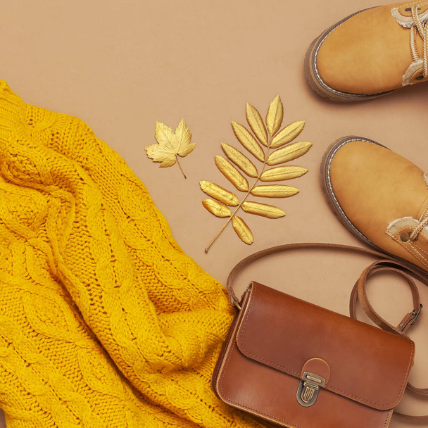 Brown leather women bag, orange knitted sweater, warm boots, golden autumn leaf on brown background top view flat lay. Fashionable women's accessories. Autumn Fashion Concept. Stylish Lady Clothes - Photo, Image