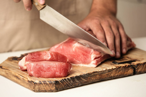 Man cutting fresh raw meat on table, closeup - Фото, изображение