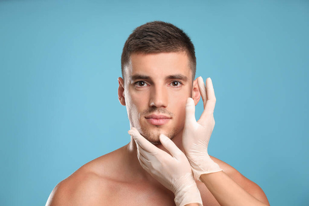 Doctor examining man's face for cosmetic surgery on light blue background - Fotografie, Obrázek