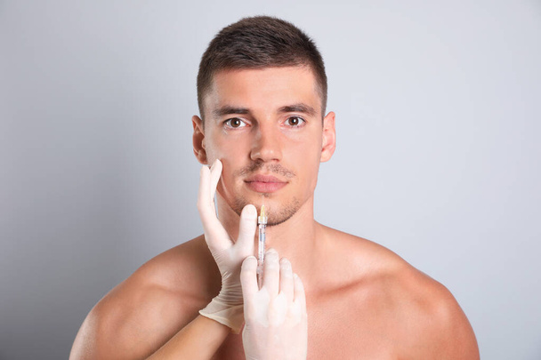 Man getting facial injection on grey background. Cosmetic surgery - Фото, зображення