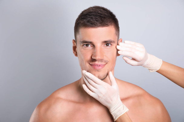 Doctor examining man's face for cosmetic surgery on grey background - Fotografie, Obrázek