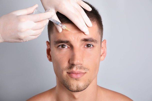 Man getting facial injection on grey background, closeup. Cosmetic surgery - Fotografie, Obrázek