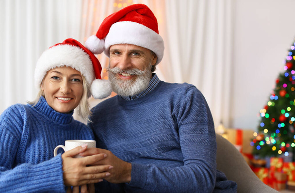 Happy couple in Santa hats celebrating Christmas at home - Fotoğraf, Görsel