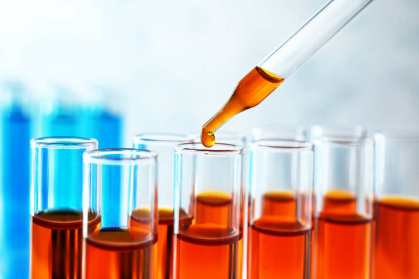 Dropping sample into test tube with orange liquid, closeup - Фото, изображение