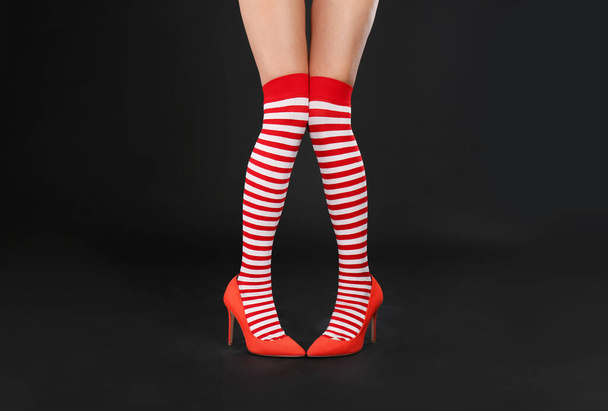 Woman wearing high heeled red shoes and festive socks against black background, closeup on feet. Christmas celebration - Photo, image