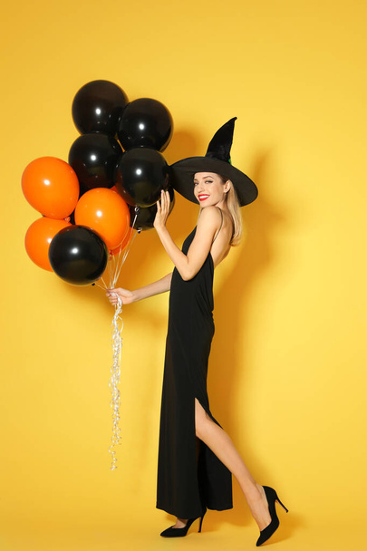 Beautiful woman wearing witch costume with balloons for Halloween party on yellow background - Fotografie, Obrázek