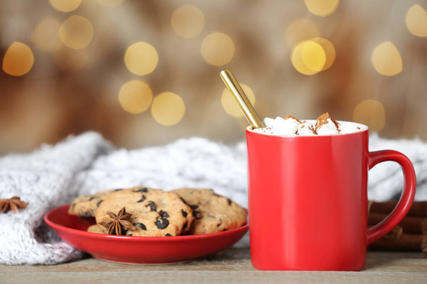 Cup of tasty cocoa with marshmallows and cookies on wooden table against blurred lights - Photo, image
