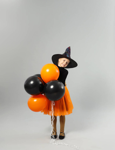 Cute little girl with balloons wearing Halloween costume on grey background - Фото, зображення