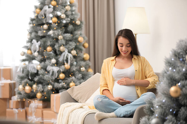 Happy pregnant woman on sofa in living room decorated for Christmas. Expecting baby - Фото, зображення