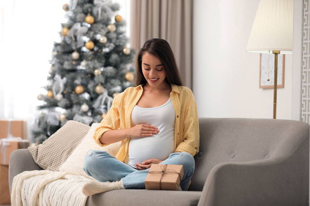 Happy pregnant woman with Christmas gift box at home. Expecting baby - Fotó, kép
