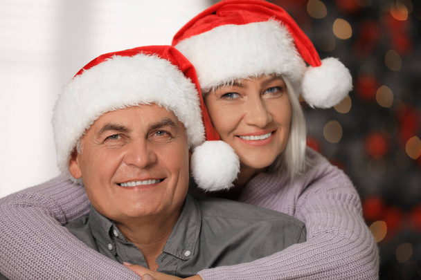 Happy mature couple in Santa hats at home. Christmas celebration - Photo, Image