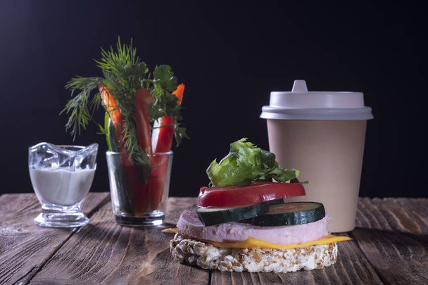 Sandwich with chopped vegetables and sauce and a cup of coffee on a wooden table and black background. - Fotoğraf, Görsel
