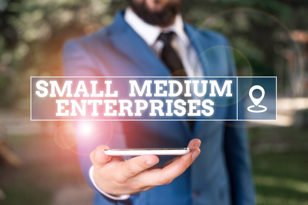 Küçük Medium Enterprises 'ın el yazısı. Kavram demek, binlerce çalışanı olan şirketlerin mavi süitteki iş adamı ellerinde cep telefonuyla ayakta durması demek.. - Fotoğraf, Görsel