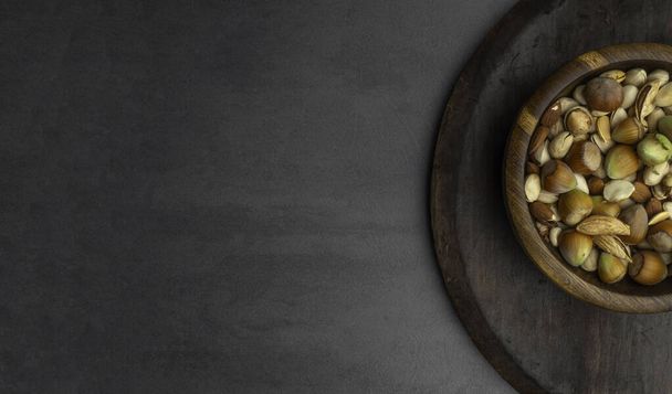 nuts and seeds in a bowl on a dark brown wooden background in a dark key - Φωτογραφία, εικόνα
