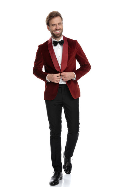 novio sonriente arreglando abrigo de terciopelo rojo sobre fondo blanco
 - Foto, Imagen