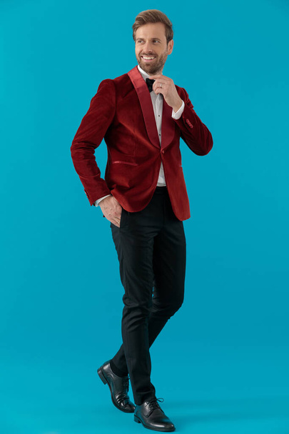 happy fashion man wearing red velvet tuxedo and fixing bowtie - Foto, afbeelding