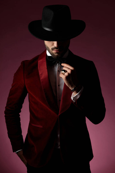 mysterious fashion man wearing red velvet tuxedo and fixing bowt - Фото, изображение