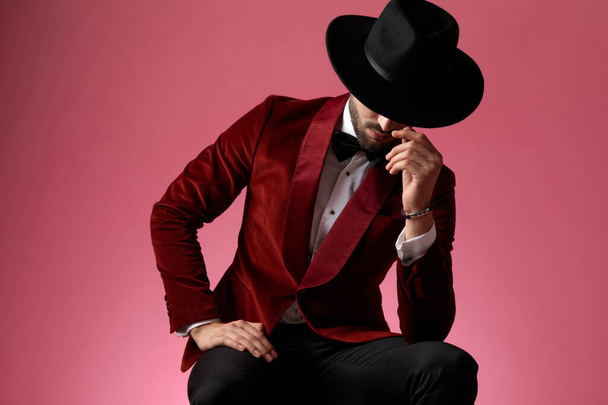 young elegant man in red velvet tuxedo covering face with hat - Photo, Image