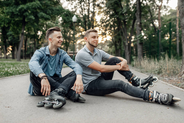 Patinagem, dois patinadores masculinos sentados no chão no parque. Patinação urbana em patins, esporte extremo ativo ao ar livre, patinação em patins
 - Foto, Imagem