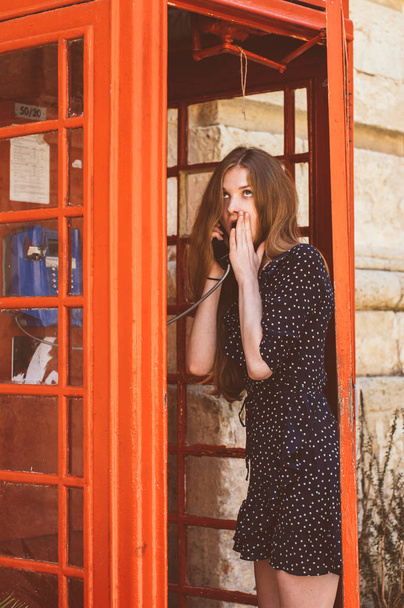 Young woman in telephone cabin talking on the phone and surprisi - Foto, imagen