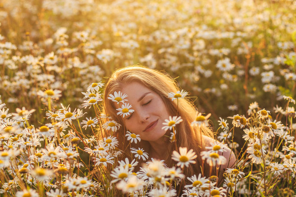 Portrait of pretty blond woman sitting in chamomile field - Foto, Imagen