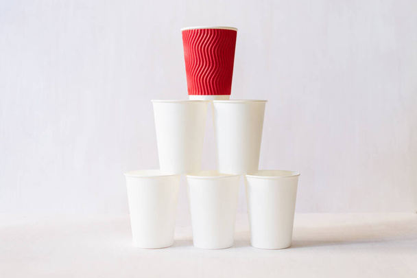 Red paper cup stands on top of white paper cups pyramid - Photo, Image