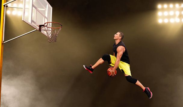 Basketball player makes a throw, shoot in jump, dark background. Male athlete in sportswear scores on streetball training - Fotoğraf, Görsel